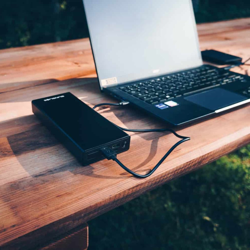 tragbares Laptop-Ladegerät, das einen Computer auf einem Tisch im Freien auflädt