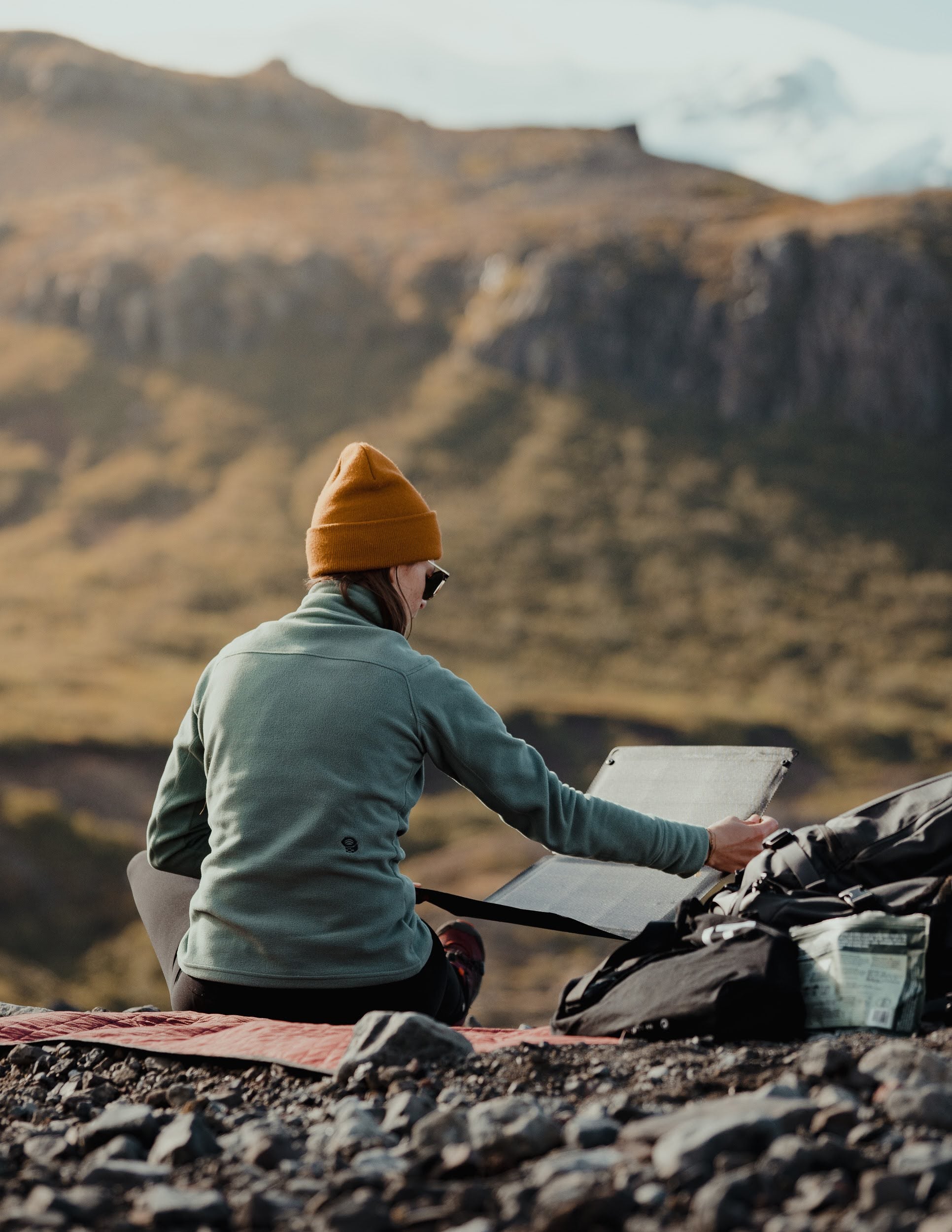 woman tilting a portable solar panel on a sunny mountain