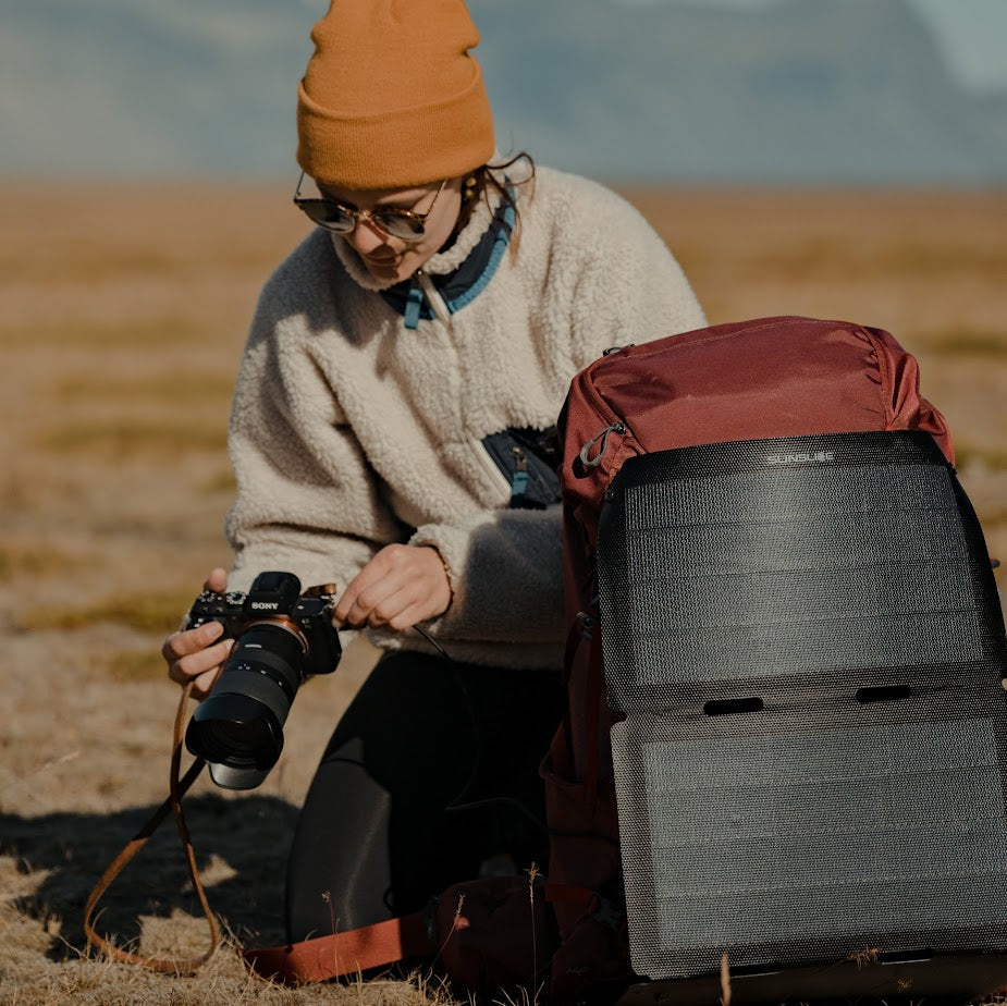 Frau schaut auf ihre Kamera mit einem Solarmodul (fusion flex 18), das an ihrem Rucksack befestigt ist