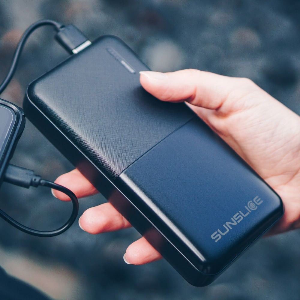 eine schöne 20000MaH-Powerbank, die von einer Hand in einem sonnigen Wald gehalten wird