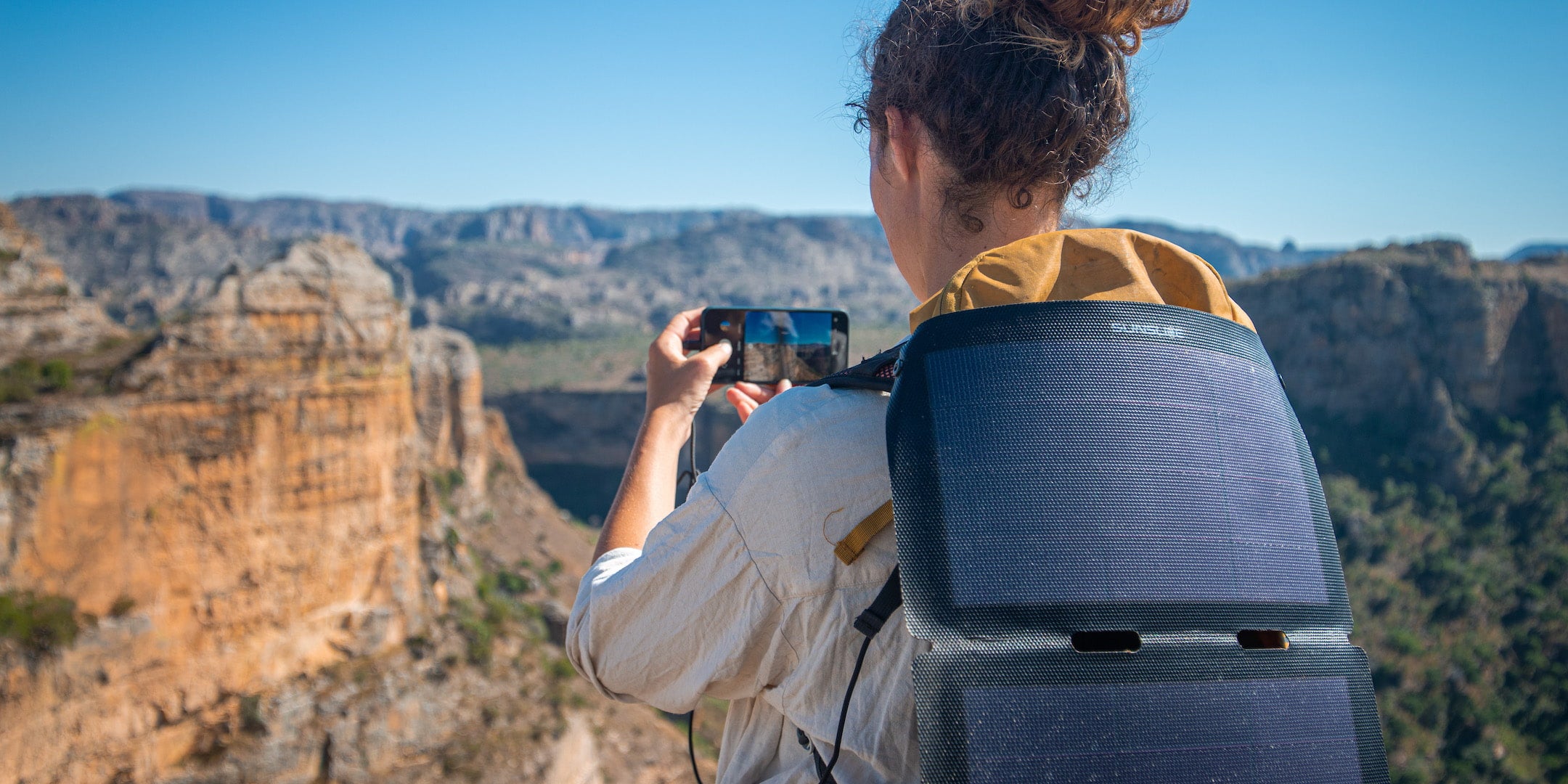 Femme prenant une photo lors d'une randonnée à Madagascar et rechargeant son téléphone à l'aide d'un panneau solaire portable de sunslice