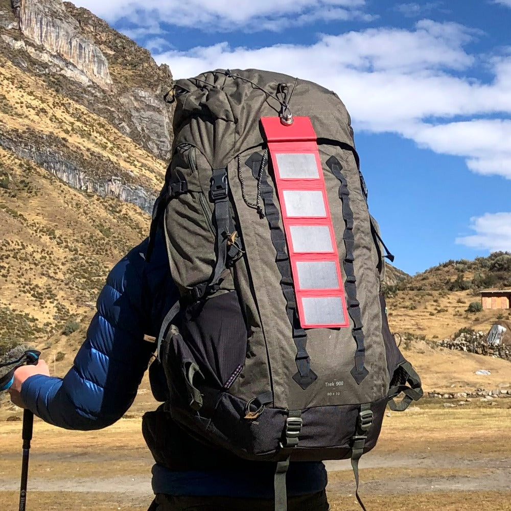un homme s'apprêtant à escalader une montagne avec un sac à dos de randonnée auquel est attaché un chargeur à énergie solaire