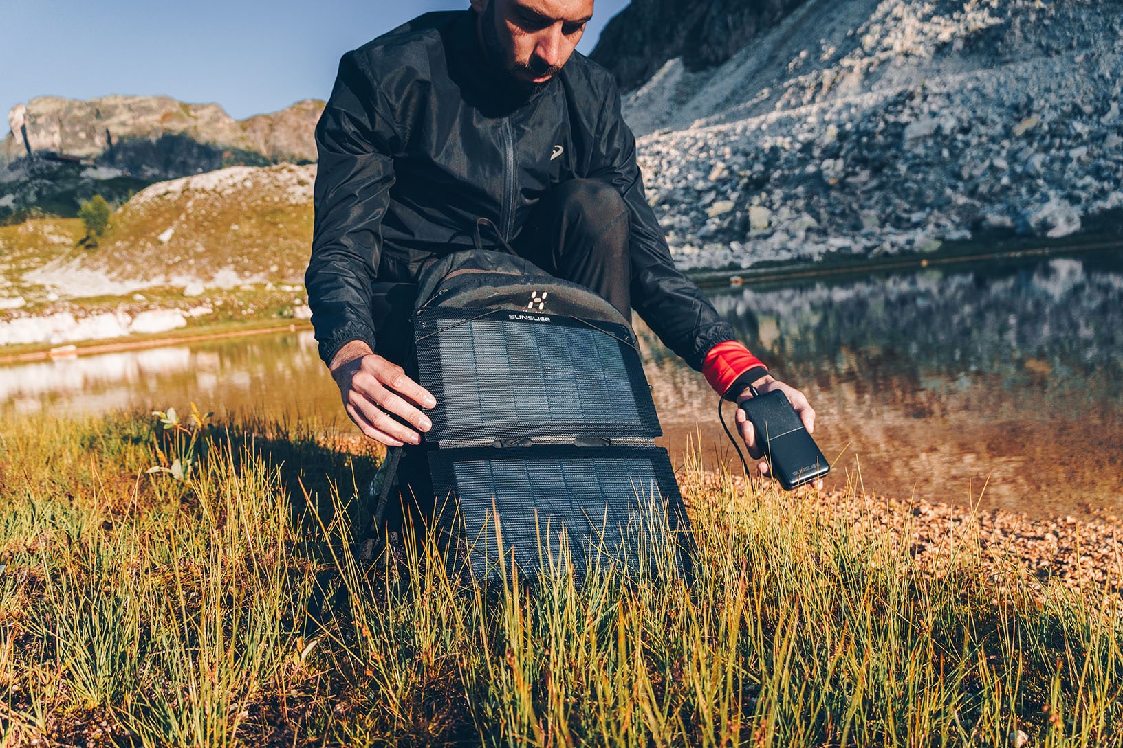 Tragbares Solarmodul ( Sunslice fusion flex 12) und eine Powerbank ( gravity 20) in der Hand eines Mannes