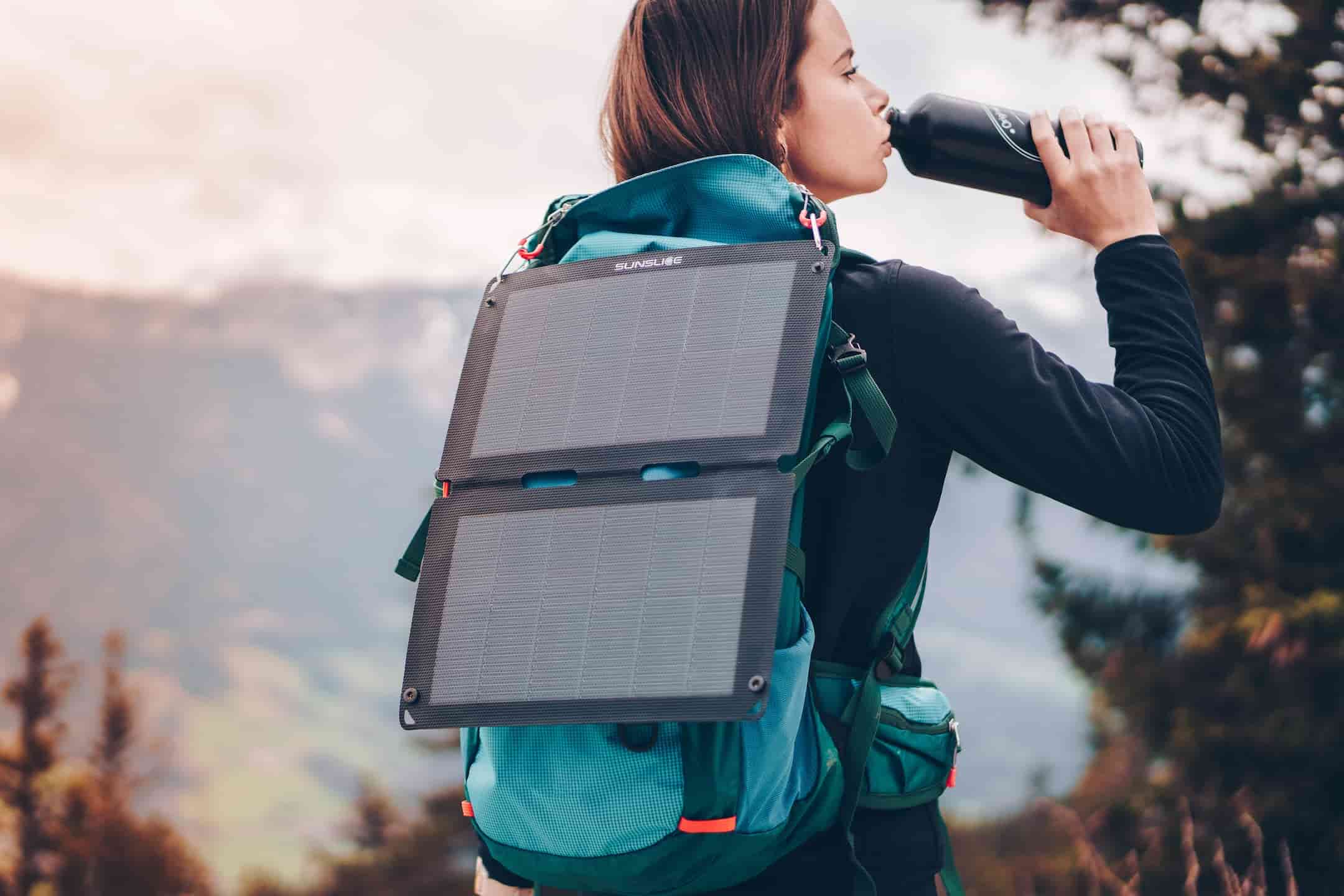 Frau trinkt Wasser aus einem Kürbis und trägt ein faltbares Solarpanel auf ihrem Rucksack