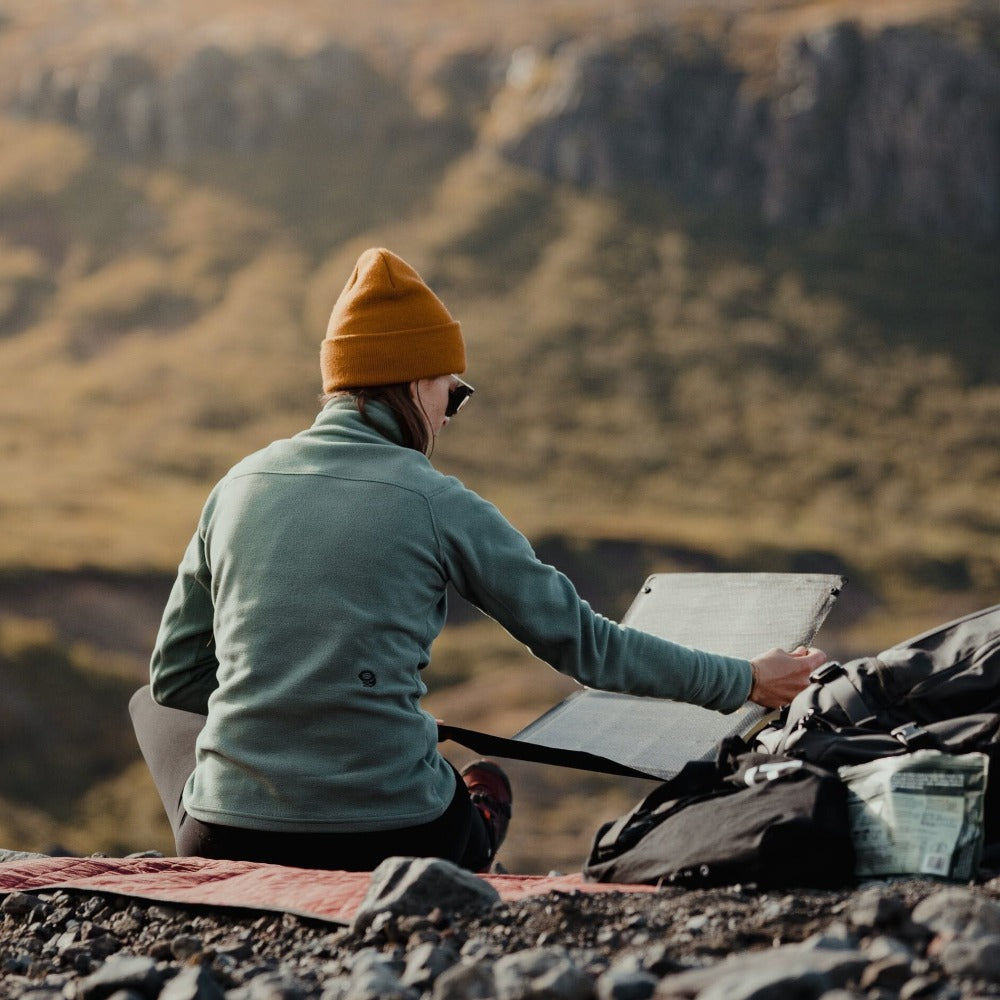 woman tilting a portable solar panel on a sunny mountain