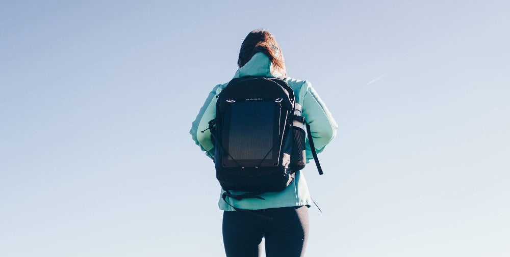 woman tilting a portable solar panel on a sunny mountain
