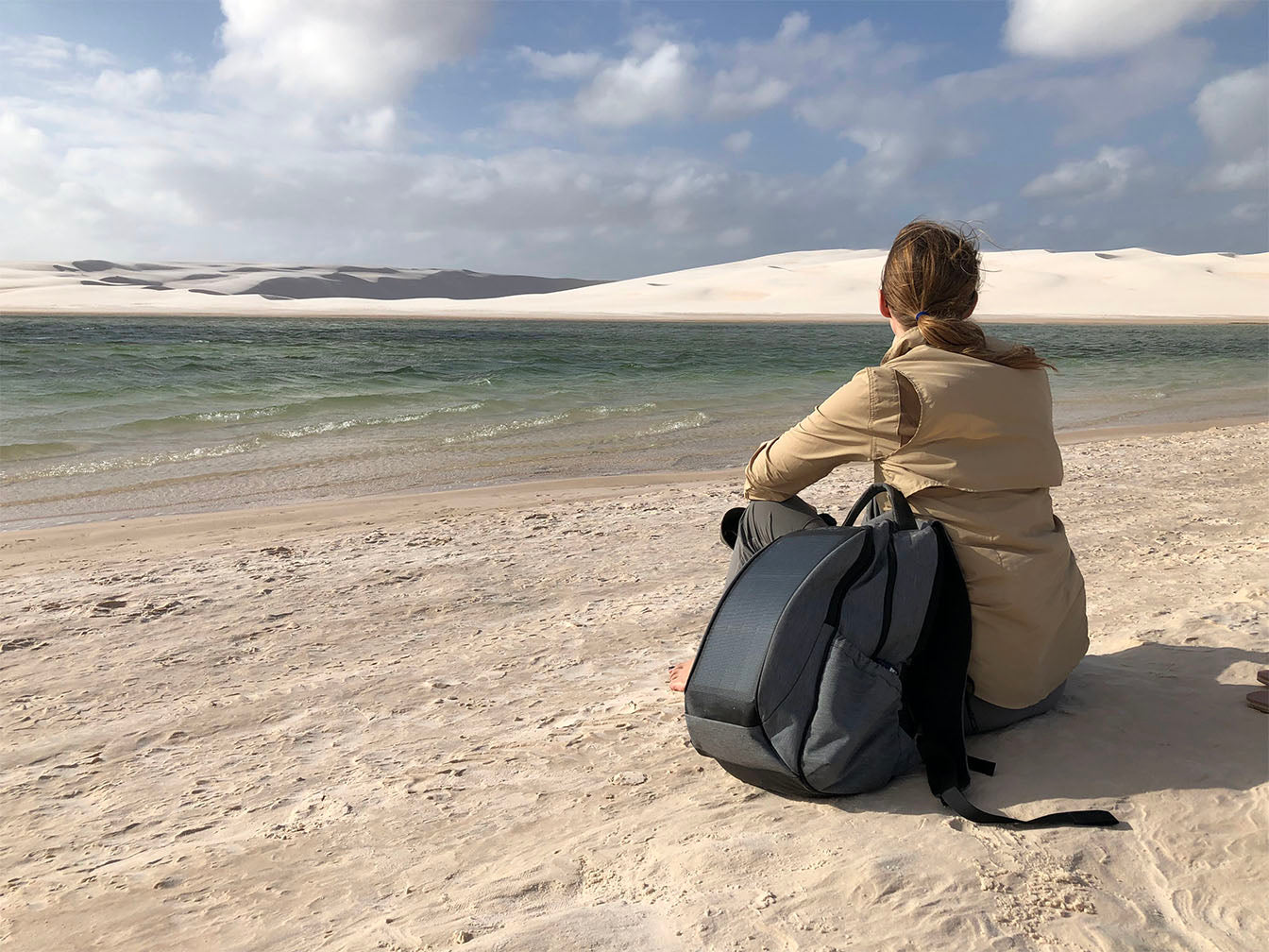A women on a beatch with a solar backpack next to her