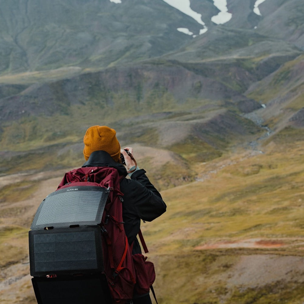 Frau, die ein Foto mit einem an ihrem Rucksack befestigten Wandersolarmodul auf dem Boden machen will