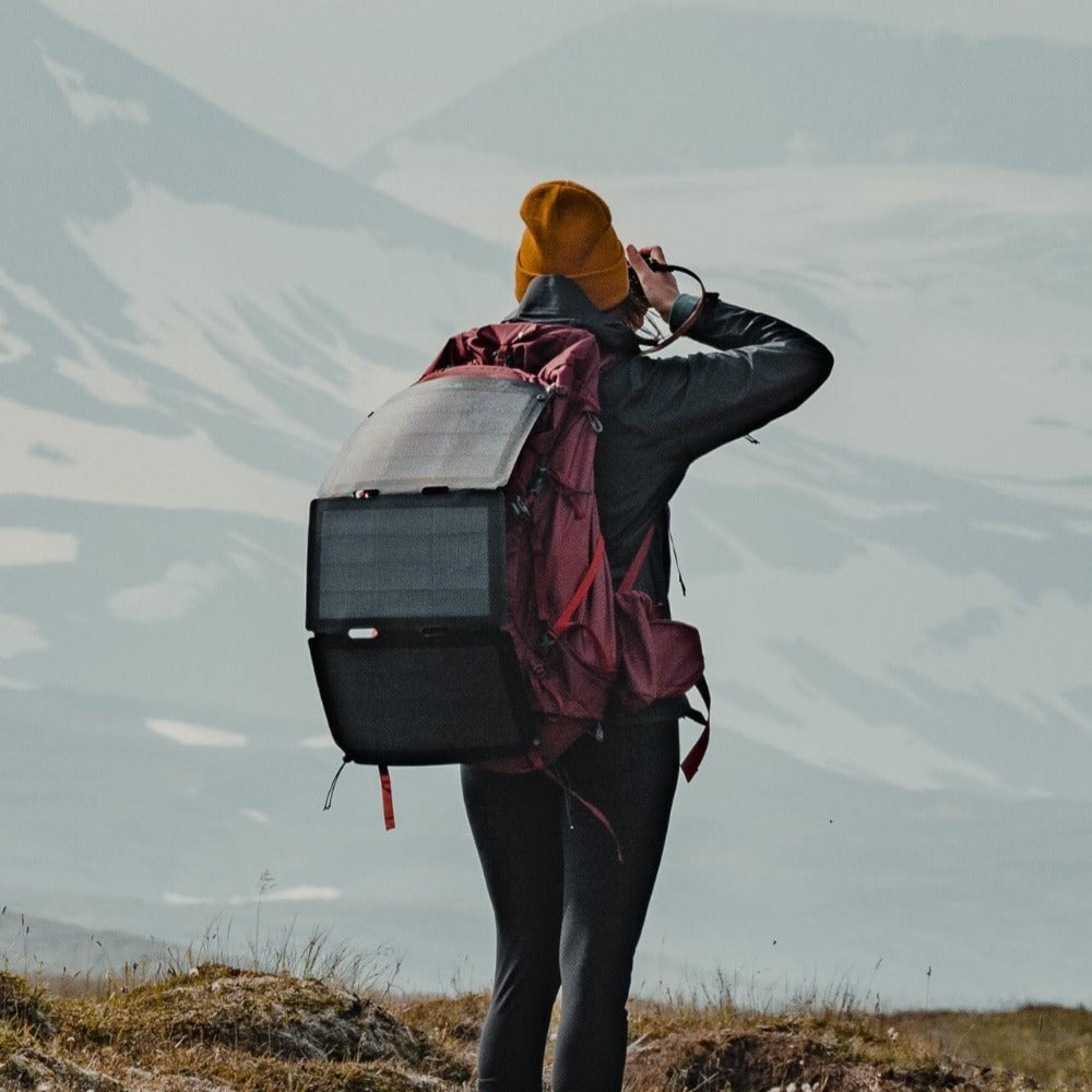 Frau, die ein Foto mit einem an ihrem Rucksack befestigten Wandersolarmodul auf dem Boden machen will