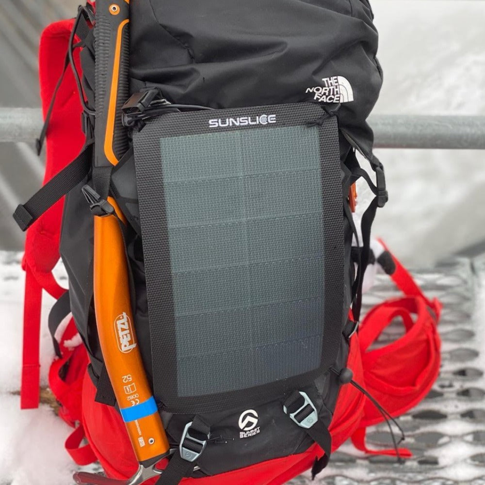 sac de randonnée posé au bord d'un ruisseau, auquel est attaché un panneau solaire portable pour le camping