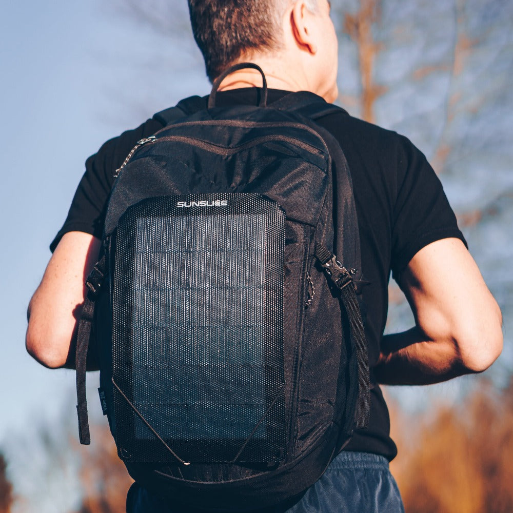 un homme au sommet d'une montagne ensoleillée avec des panneaux solaires de randonnée attachés à son sac à dos