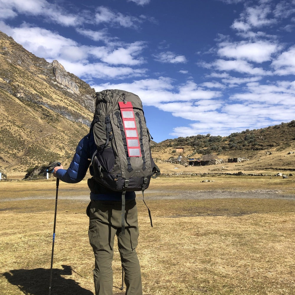 un homme s'apprêtant à escalader une montagne avec un sac à dos de randonnée auquel est attaché un chargeur à énergie solaire