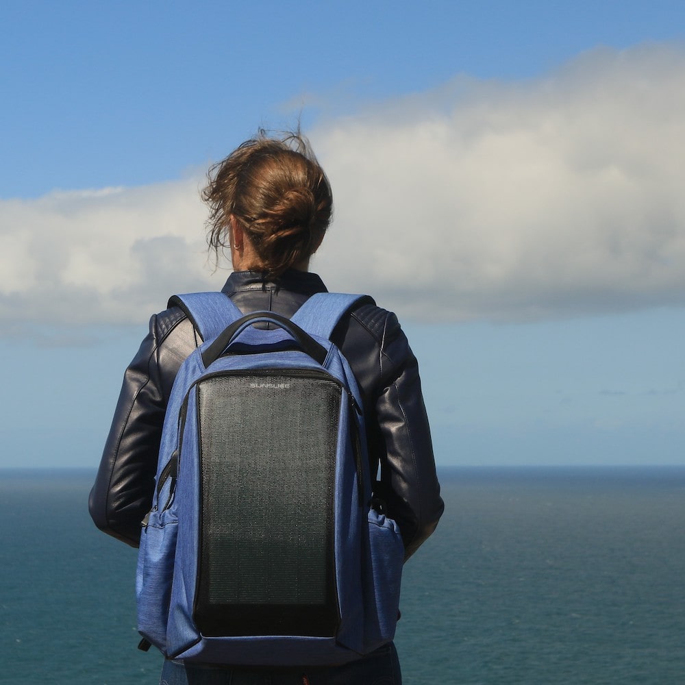 Woman wearing a Blue Zenith solar backpack in front of the ocean