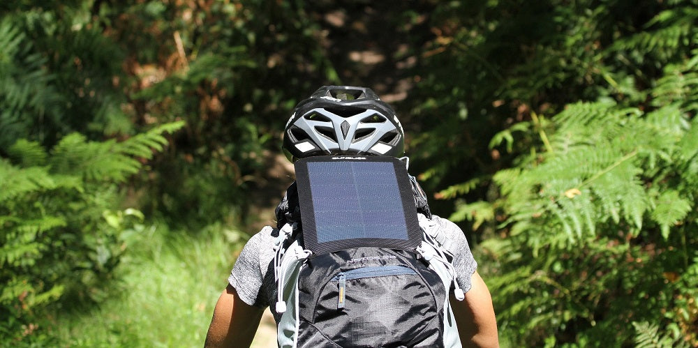 homme faisant du vélo avec un panneau solaire compact attaché à son sac à dos