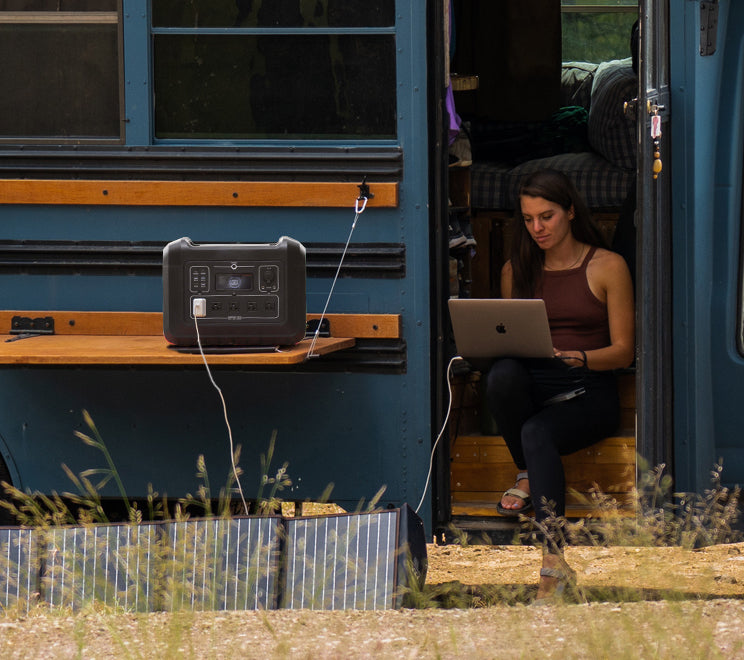 Frau, die in einem Wohnmobil reist, lädt ihren Computer mit einem Solargenerator für zu Hause auf