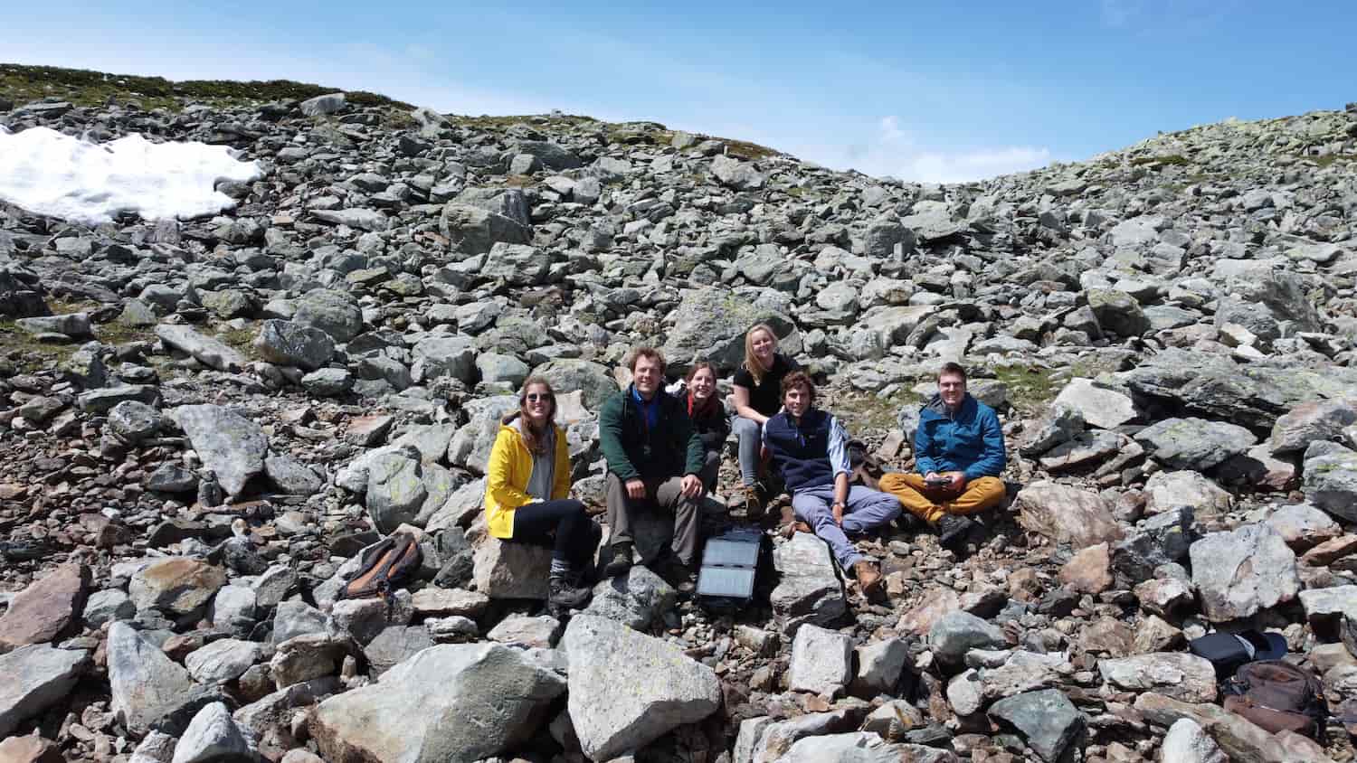 group photo of tourists on a sunny rocky mountain with a hiking solar panels