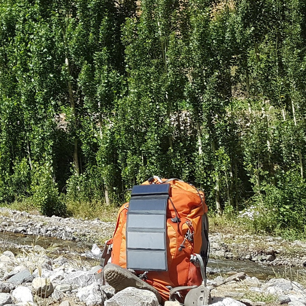 hiking bag with Electron solar charger placed beside a watercourse 