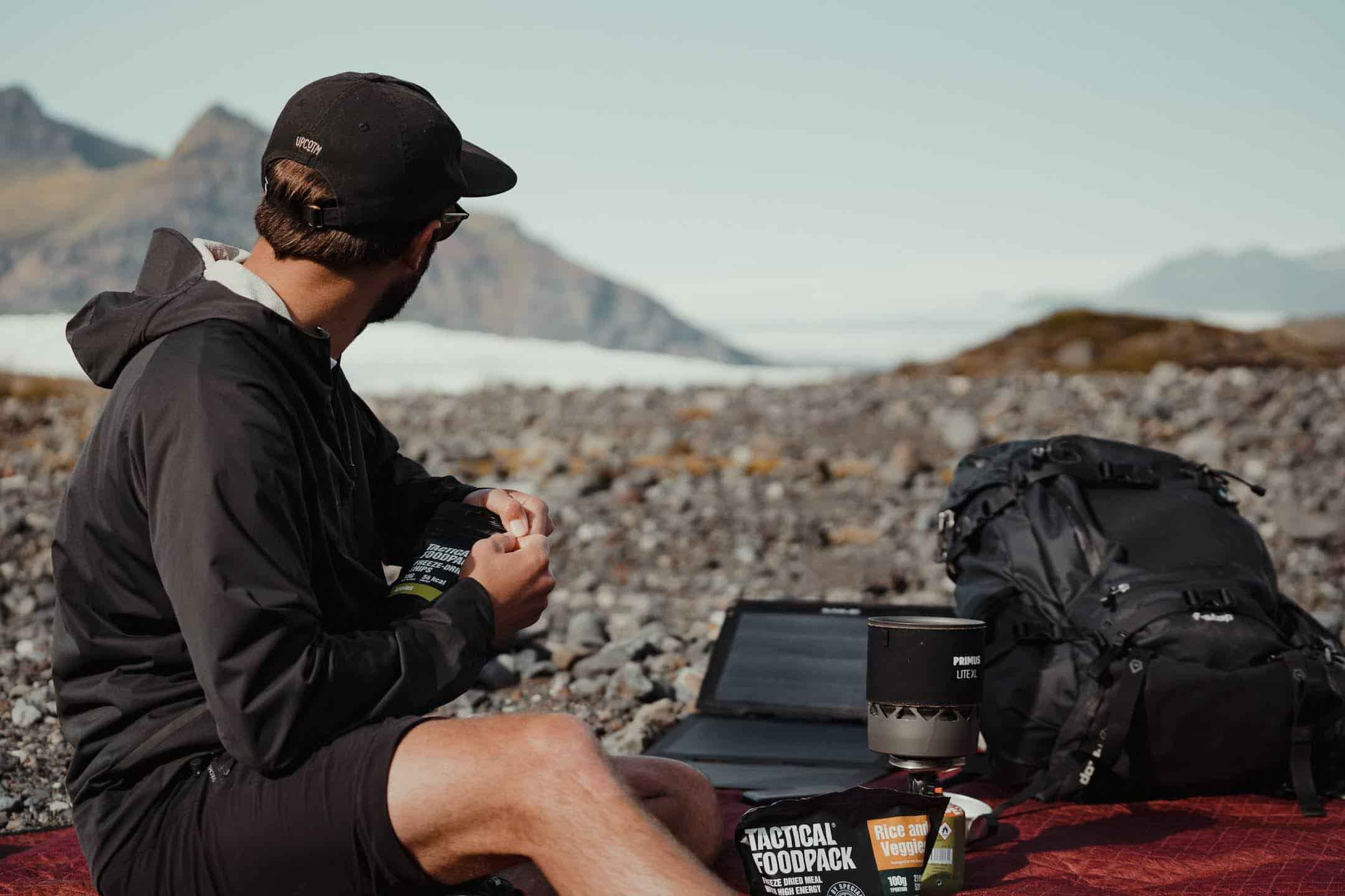 Mann, der mit einer professionellen Kamera in der Hand und einem tragbaren Solarmodul für Campingzwecke auf den Horizont blickt