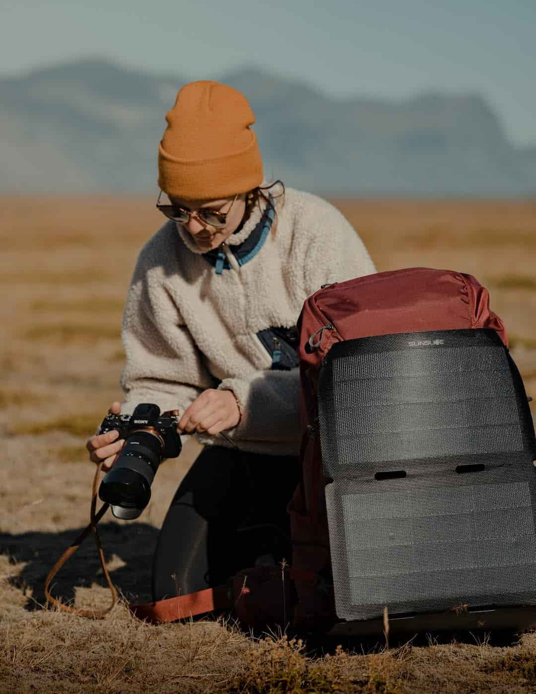woman about to take a photo with a hiking solar panels attached to her backpack on the ground