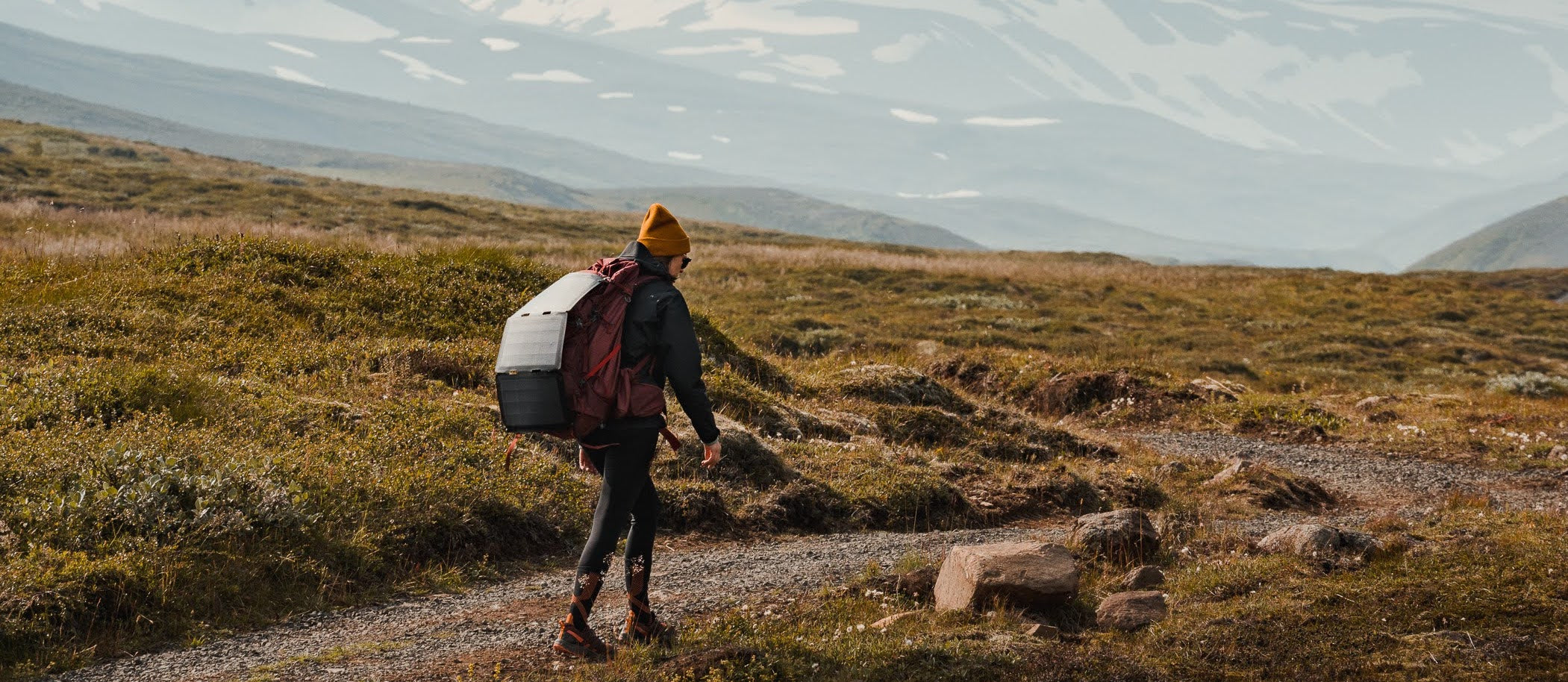 Frau beim Wandern mit einem tragbaren Solarmodul für das Camping, das an ihrem Rucksack befestigt ist 