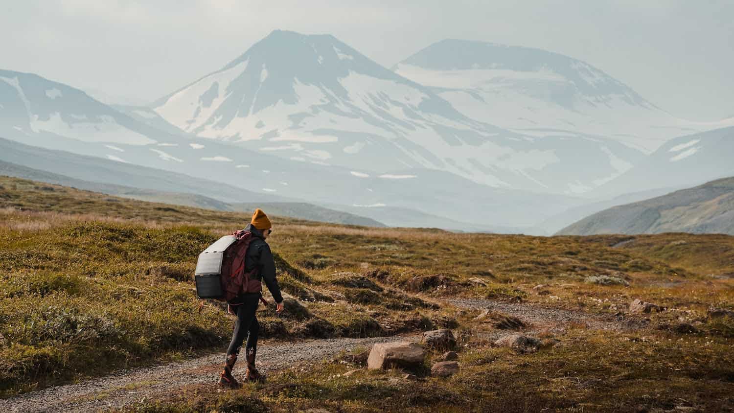 woman walking on a rocky path with a backpack and solar power pack plugged in.