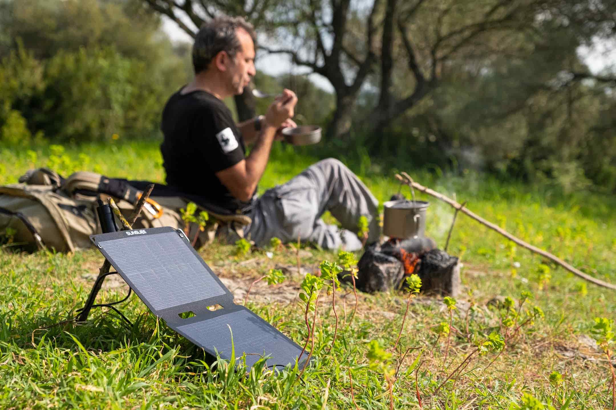 man on a hike having lunch and his portable solar panel charging in the sun