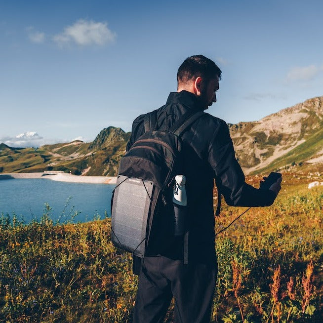 man on top of a mountain with the best portable solar panel attached to his hiking backpack