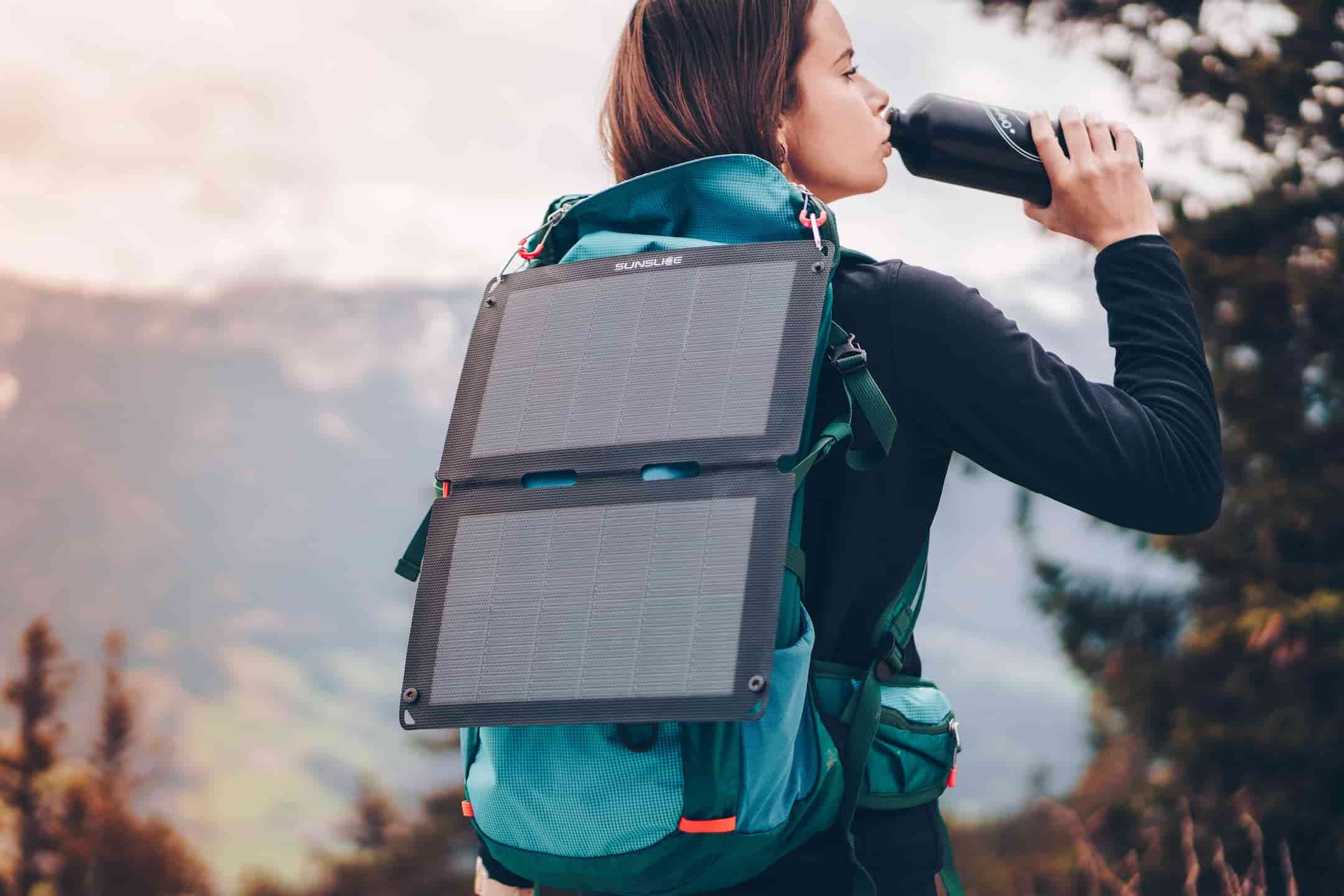 woman drinking water from a gourd and carrying a foldable solar panel on her backpack