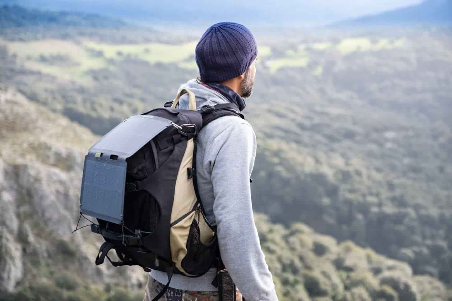 homme au sommet d'une montagne avec le meilleur panneau solaire portable attaché à son sac à dos de randonnée