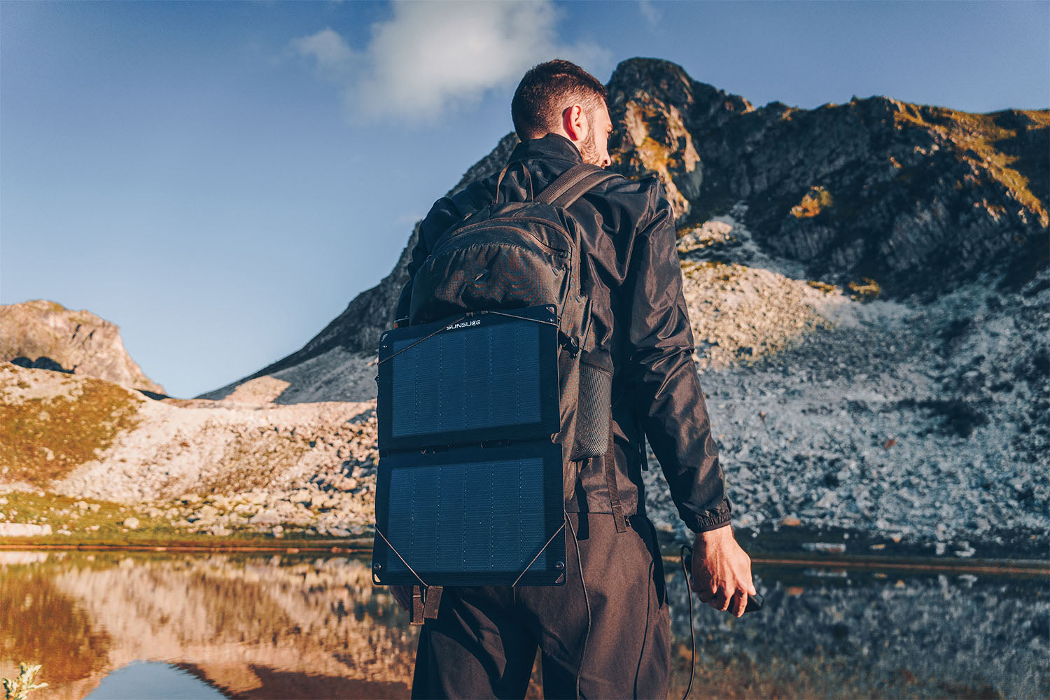 Man standing with a backpack where a portable solar panel ( Fusion 12) is attatched