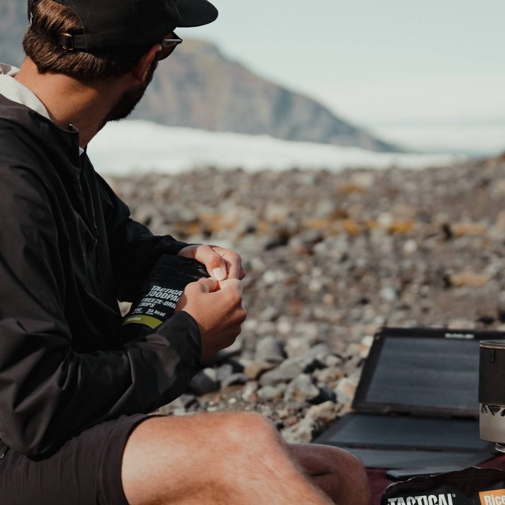man gazing at the horizon with professional camera in hand and portable solar panel for camping at his side