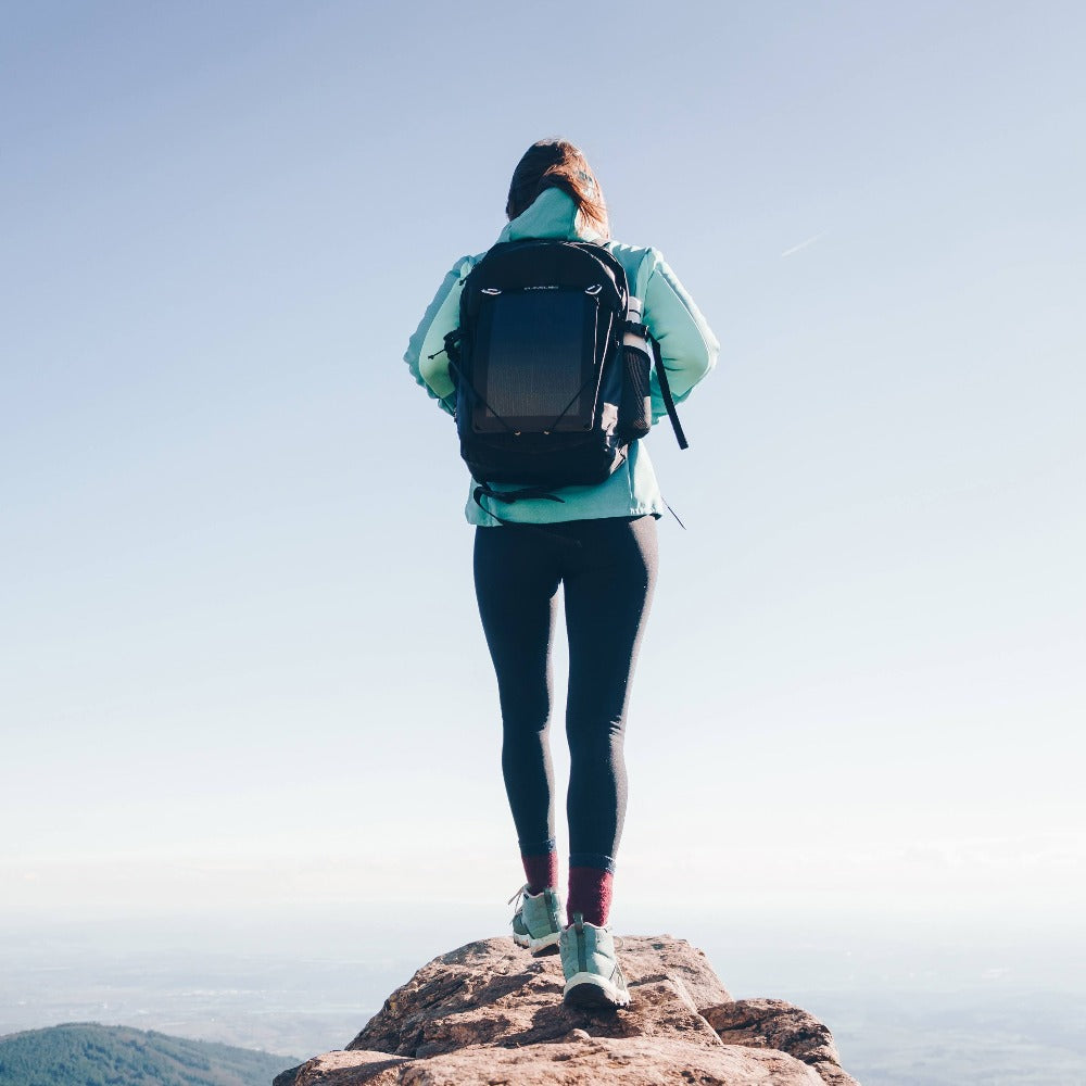 woman tilting a portable solar panel on a sunny mountain