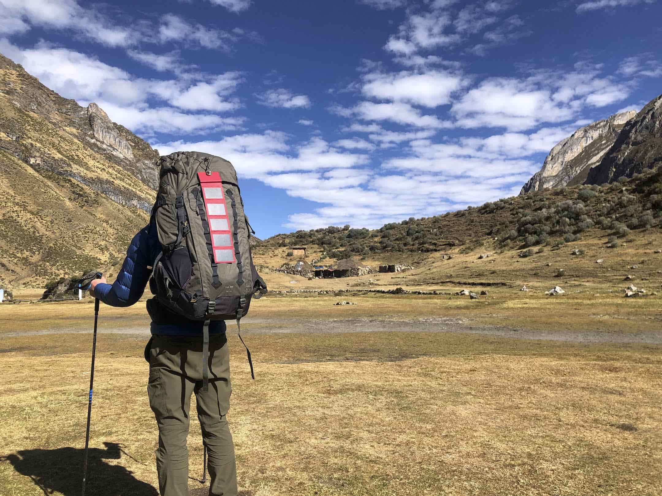 man hiking under a beautiful blue sky with a power bank for camping attached to his pack