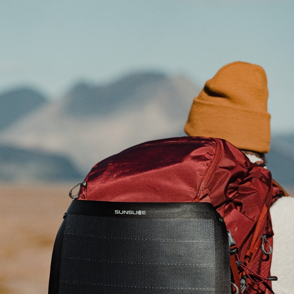 Frau beim Wandern mit einem tragbaren Solarmodul für das Camping, das an ihrem Rucksack befestigt ist 