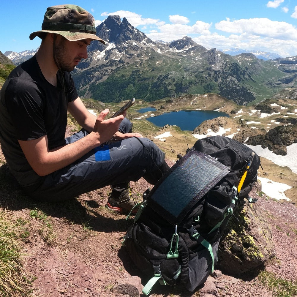 un homme au sommet d'une montagne ensoleillée avec des panneaux solaires de randonnée attachés à son sac à dos