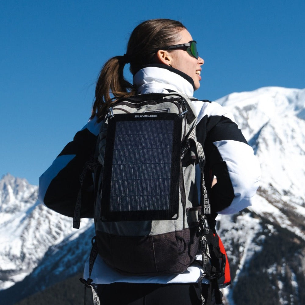 vrouw die een draagbaar zonnepaneel op een zonnige berg kantelt