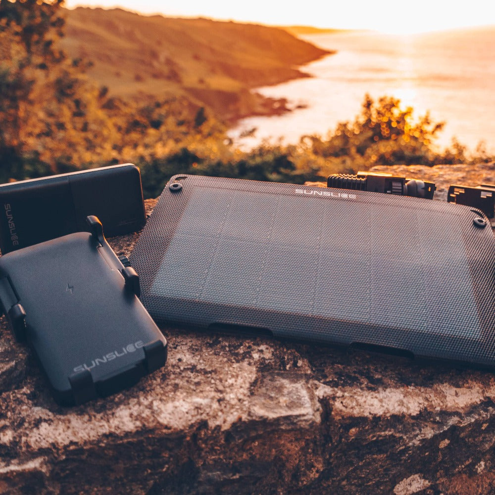 ein Camper auf einem Berggipfel, der ein tragbares Solarpanel für das Camping mit einer Powerbank präsentiert 