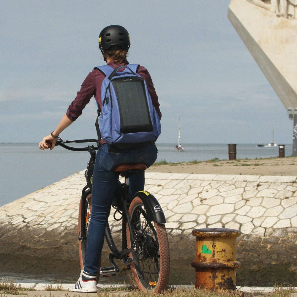 Mann auf dem Fahrrad mit einem kompakten Solarpanel, das an seinem Rucksack befestigt ist